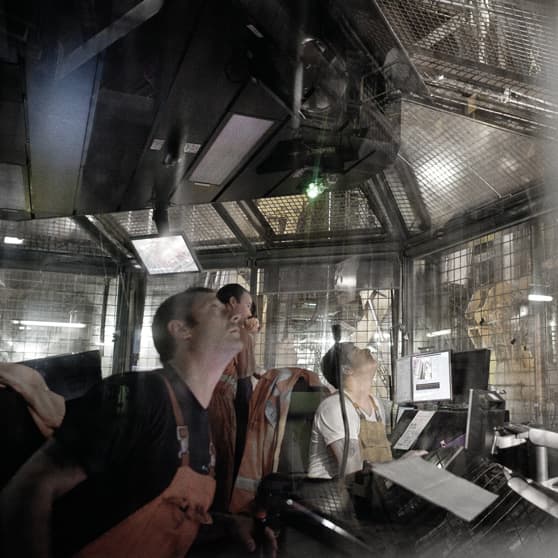 Control Room Observation: Individuals inside a control room closely monitor equipment and screens, focusing on operational tasks within a secured and industrial environment.